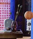 Vase of poppy seed heads next to china jar and lantern