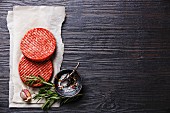 Raw Ground beef meat Burger steak cutlets and seasonings on black burned wooden background
