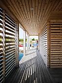 Slatted wooden arcade surrounding floating wooden house; pattern of light and shade