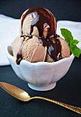 Three scoops of homemade chocolate gelato with chocolate sauce in a white bowl