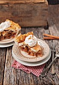 Slice of double crust apple pie with whipped cream and cinnamon on a rustic wooden surface