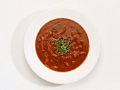 A bowl of tomato and onion soup in front of a white background (seen from above)