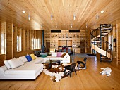 Open-plan interior of wooden house with elegant lounge area, spiral staircase and fitted shelving