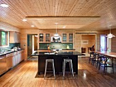 Black kitchen counter and bar stools in open-plan kitchen in bright, renovated wooden house