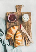 Freshly baked croissants with raspberry jam and milk in bottle on rustic wooden board