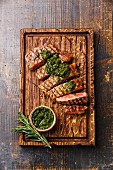 Sliced medium rare grilled beef Sirloin steak with chimichurri sauce on cutting board on wooden background