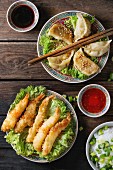 Fried tempura shrimps and gyozas potstickers on lettuce salad with sauces and rice