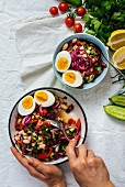 A woman is stirring a tangy and colorful Turkish bean salad known as piyaz in a large bowl and a small bowl, herbs, lemon, cherry tomatoes