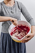 A woman holding a large bowl and mixing a a red velvet cake batter
