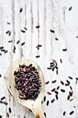 Black rice on a spoon and a wooden background (seen from above)