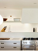 White wall-mounted shelves, indirect lighting and gas hob in kitchen
