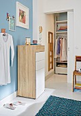 A chest of drawers in front of a light blue wall in a bedroom with a walk-in wardrobe with sliding door in the background