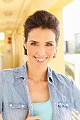 Brunette woman with backcombed hair wearing turquoise top and denim shirt