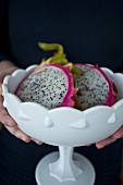 A woman holding a white dish with two dragonfruit halves