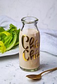 A bottle of caesar salad dressing with romaine lettuce in backround
