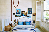 Double bed with blue pillows and portrait painting on white painted brick wall