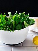 Broccolini in a white bowl, with a lemon and block of parmesan beside it
