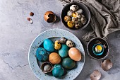 Colored Easter blue brown chicken and quail eggs, whole and broken with yolk in shell in spotted plate and black bowls