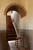 Stuhl vor dem Durchgang mit gemauertem Bogen zur Treppe