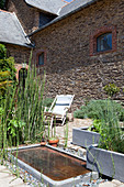 Terrasse mit Teich und Pflanzkübeln vor einem altem Steinhaus