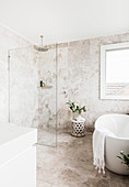 Frei stehende Badewanne und Dusche mit Glastrennwand in elegantem Badezimmer mit Kalksteinfliesen