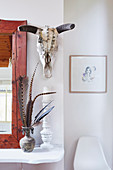 Spiegel, Vase mit Federn und Kerzenhalter auf weißer Ablage, darüber Tierschädel