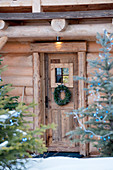 Wreath on wooden door of rustic log cabin in winter