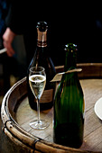 Open bottles and glass of Champagne on top of wooden barrel