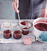 Homemade plum jam being filled into jars with a funnel
