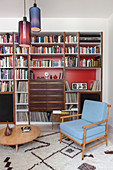 Retro armchair and round coffee table in front of bookcase with red back wall