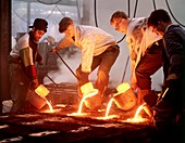 Foundry workers pouring hot metal into moulds
