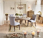 Grey upholstered chairs around silver tray on round rustic table below chandelier in period apartment