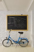 Blue folding bike below architect's plan on chalkboard