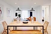 Dining table with metal frame and wooden top, wooden bench and wooden chairs in open-plan interior
