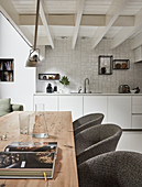 View across long wooden table and upholstered chairs into open-plan kitchen