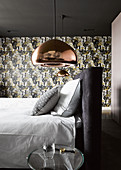 Copper-coloured ceiling lamps above bed in front of patterned wallpaper