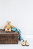 Teddy bear and checked shirt on wicker trunk next to white shoes