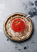Red caviar in glass bowl on ice in metal plate on concrete background