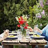 Personen beim Mittagessen an Tisch im sommerlichen Garten