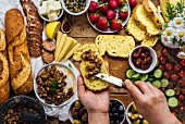 A woman spreading olive tapenade on a slice of corn bread, French baguette, sausages, baby corns, cheese, strawberries