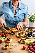 A woman slicing French baguette, olive tapenade on bread slices, olives, pickled baby corns, strawberries