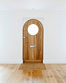 Front door with round window in empty room with oak parquet floor