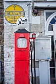 Red, English, vintage petrol pump in front of yellow enamel sign on façade
