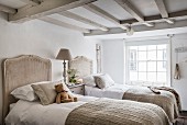 Twin beds with rattan headboards in bright, vintage bedroom with wood-beamed ceiling