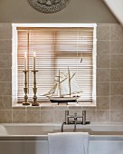 Candlesticks and model boat in front of louvre blinds on windowsill of bathroom window