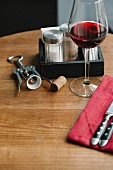 A glass of red wine, a corkscrew, cutlery, and salt and pepper shakers on a table