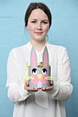 Young woman holding hand-made, paper Easter basket with bunny face