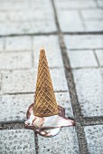 Ice cream cone with melting scoop upside down on the ground
