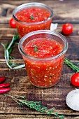 Two glasses of homemade tomato sauce and ingredients on wood