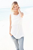 A blonde woman wearing a white top and jeans on the beach